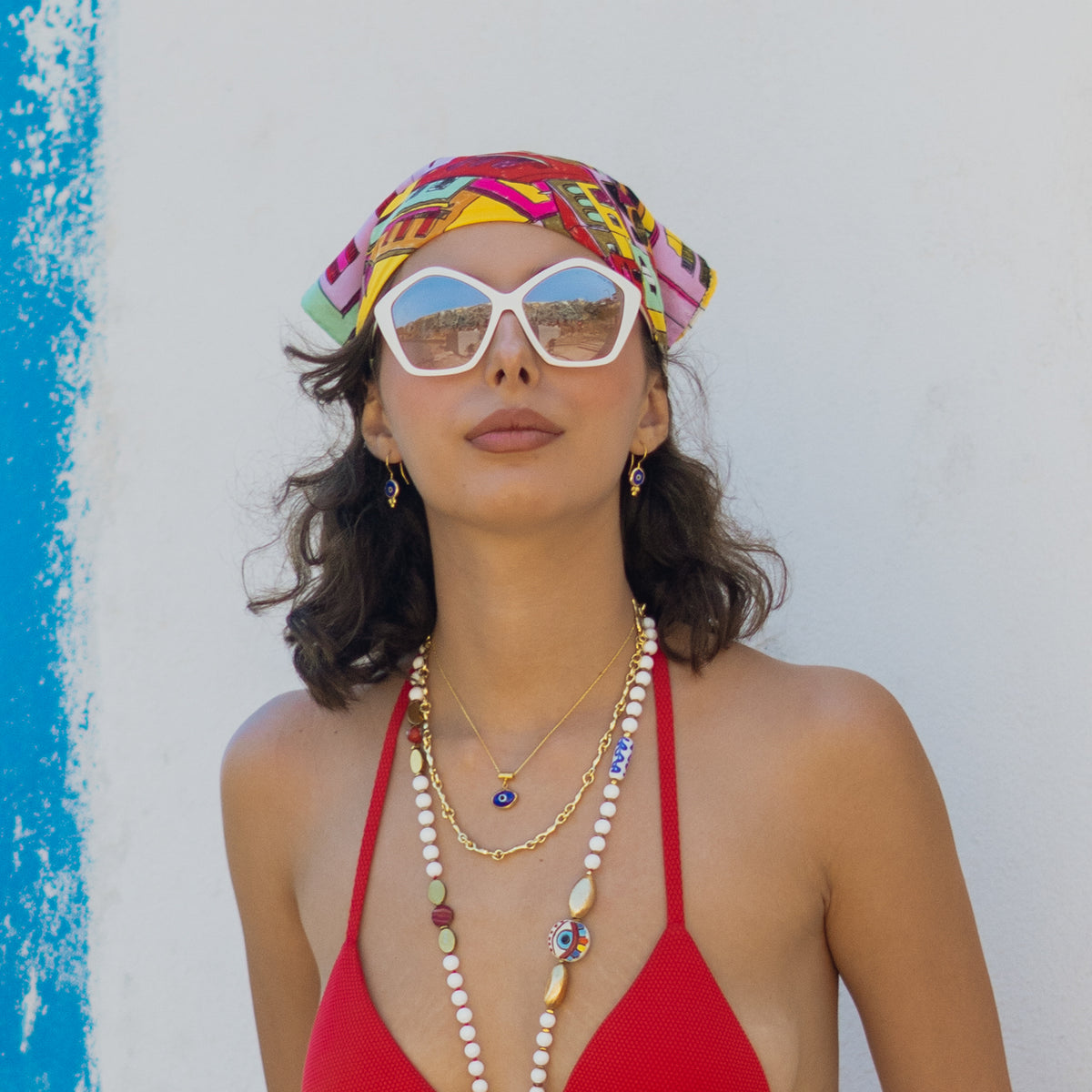 Model against a white wall wearing the Watch Over Me blue evil eye gold necklace with matching evil eye earrings