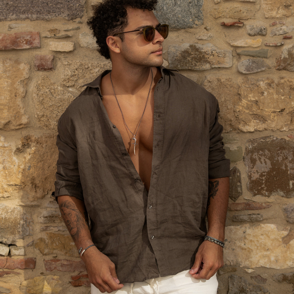 Man in a brown linen shirt against a stone wall wearing the Wolf Sword silver pendant necklace