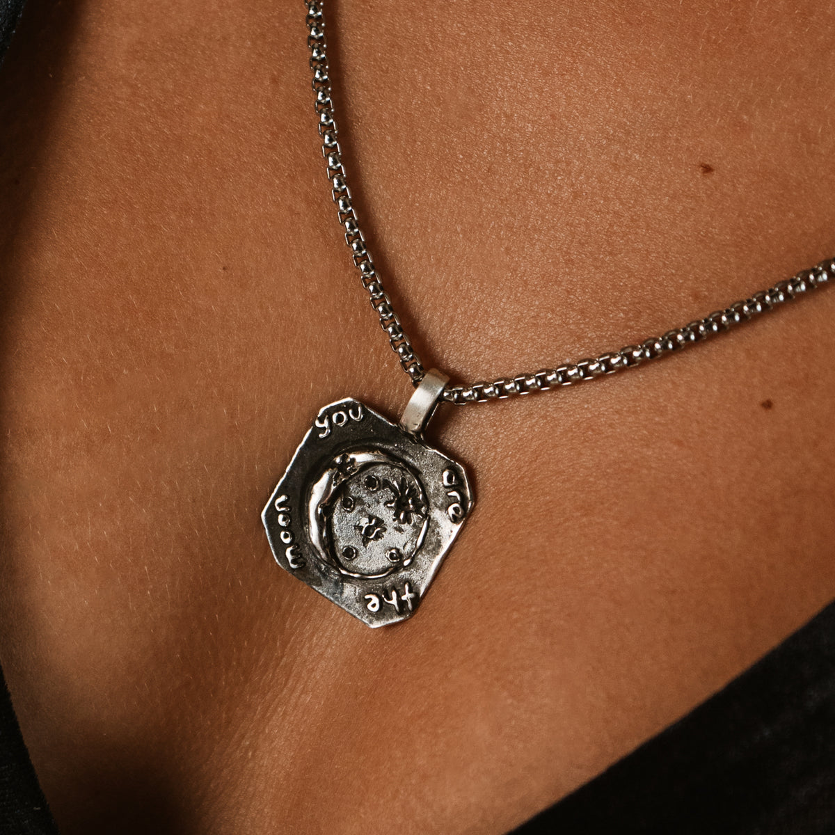 Close up of the You Are The Moon sterling silver pendant worn on skin, showing the hand worked surface and engraved words