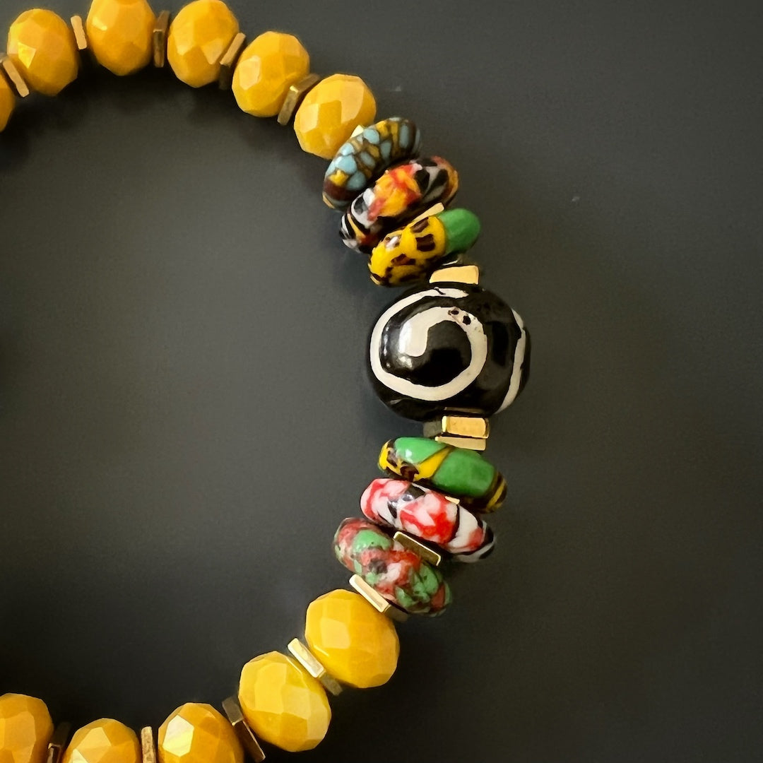 A photo of the African Yellow Women Bracelet on a black background, highlighting its unique spiral and eye Nepal beads and colorful African beads.
