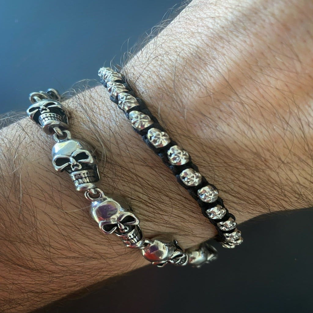 A hand model showcasing the black and silver skull bracelet with 925 Solid Sterling Silver skull charms on a black knotted rope, perfect for any biker or skull enthusiast looking for a stylish and edgy accessory.