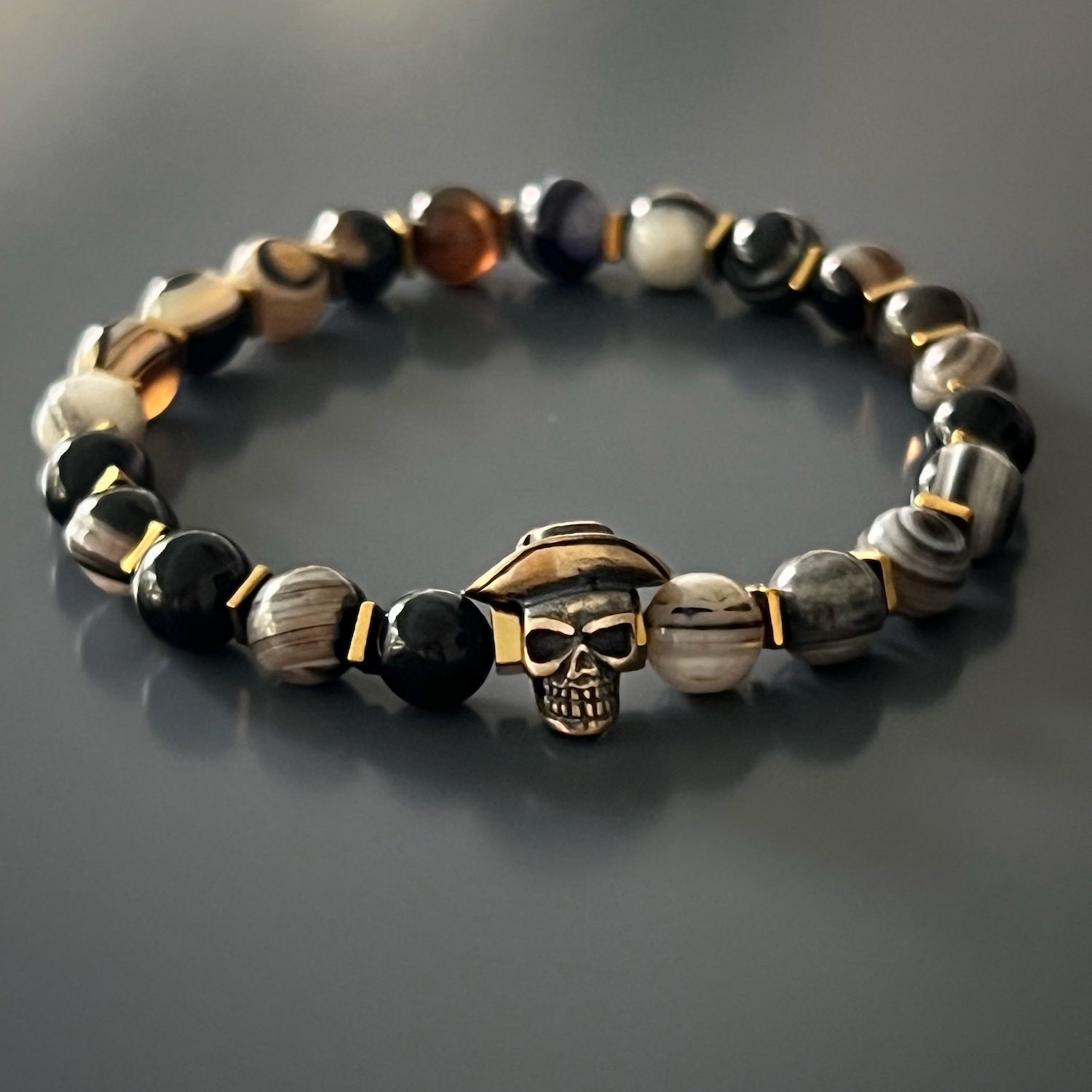 Elevate your style with the Cowboy Hat Skull Agate Bracelet. This handmade bracelet showcases Agate stone beads, gold hematite spacers, and a bronze cowboy hat skull charm. Embrace your individuality and add a touch of edginess to your accessories.