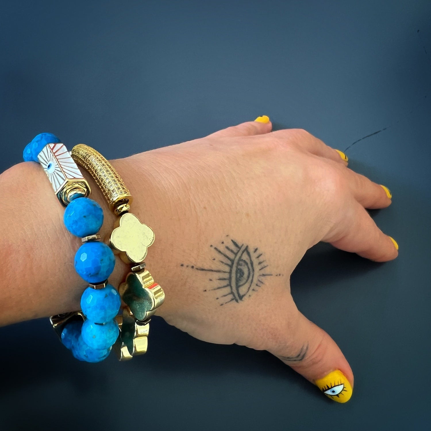A hand model wearing the Diamond and Gold Clover Bracelet, showcasing its elegant design with gold hematite clover beads, a diamond tube accent, and a stretchy jewelry cord for a comfortable fit.