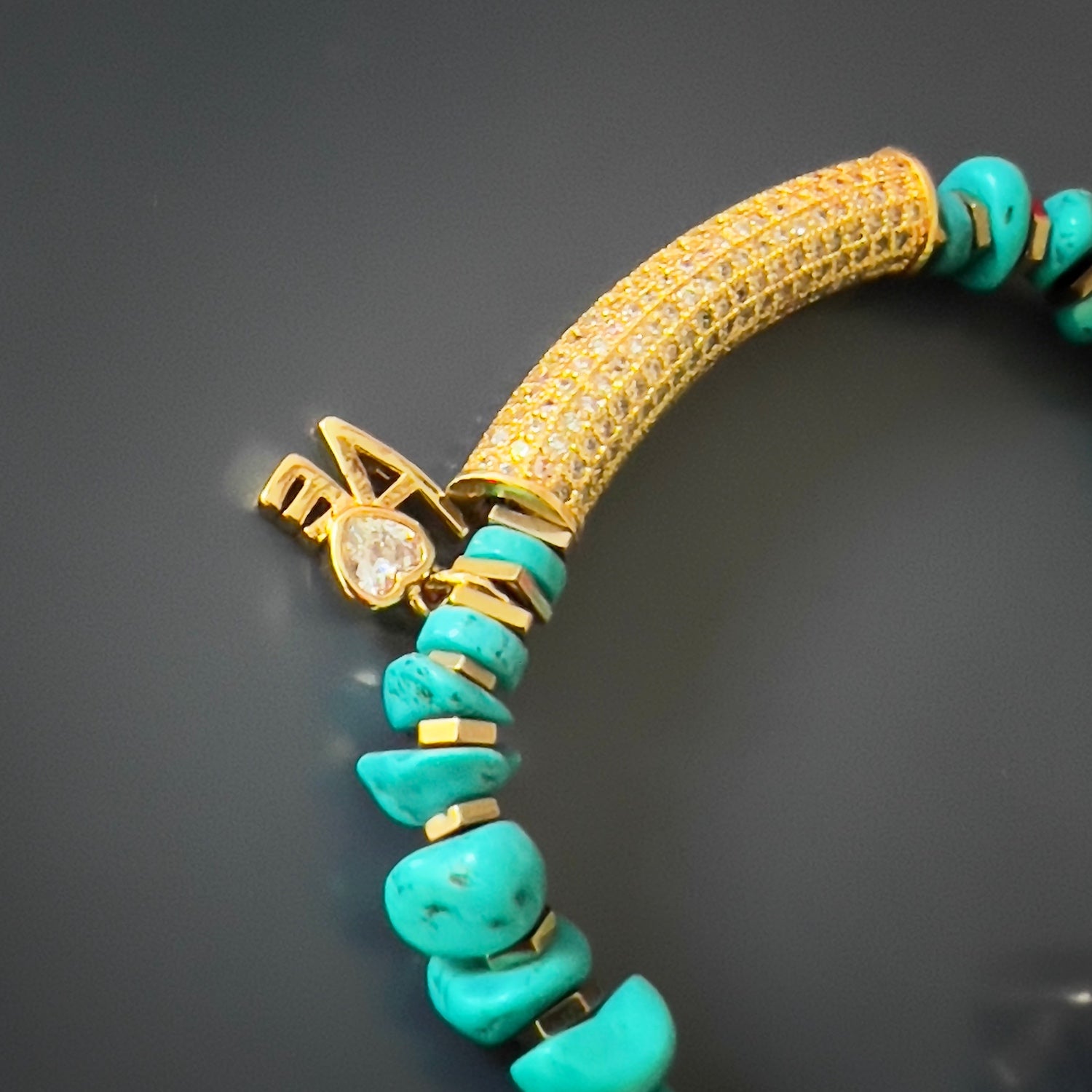 A close-up view of the Diamond and Turquoise Love Bracelet, showcasing its natural nugget turquoise stone beads, gold color hematite spacers, and a gold plated charm with a simulated diamond. The bronze bead with elephant, evil eye, and hamsa symbols adds an extra touch of protection and symbolism.