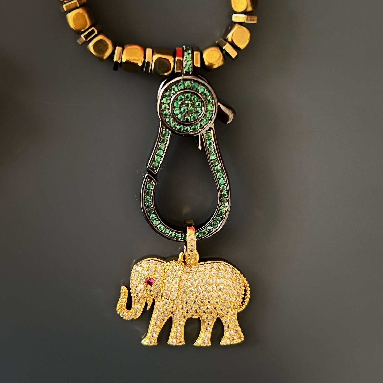 A top-down view of the Diamond Elephant Golden Necklace, displaying the elegant pendant with simulated diamonds and green jade beads against a contrasting background.