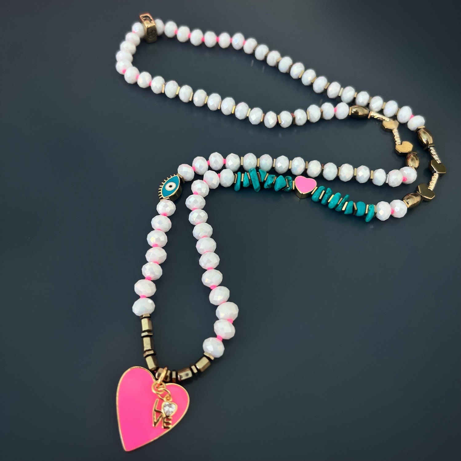 The 18K gold plated pink enamel heart pendant and love charm add a romantic touch to the design.