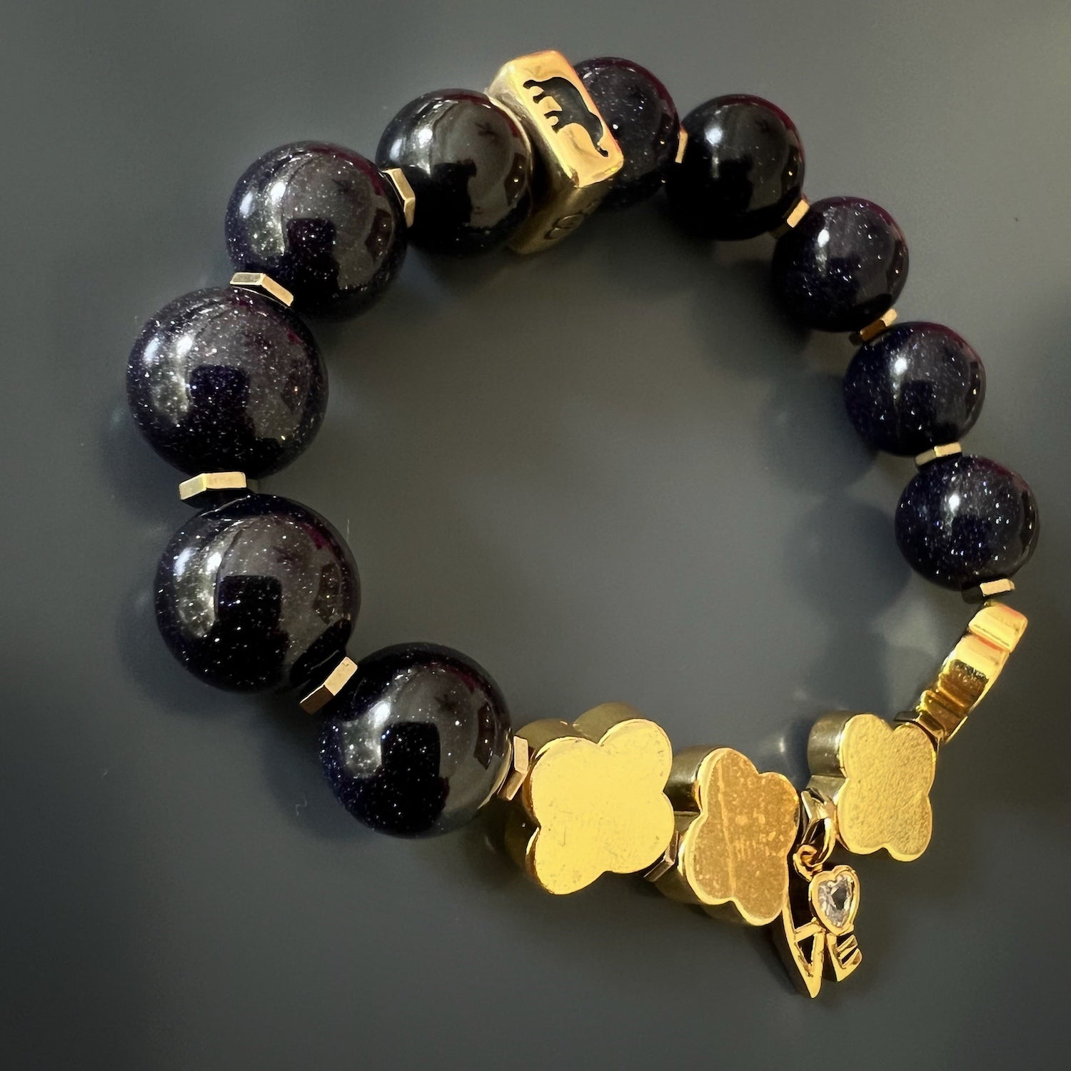 Handmade Gold Alhambra Bracelet - Striking accessory with gold hematite clover beads, gold hematite stone spacers, and an intricately designed love charm in elegant cursive writing.
