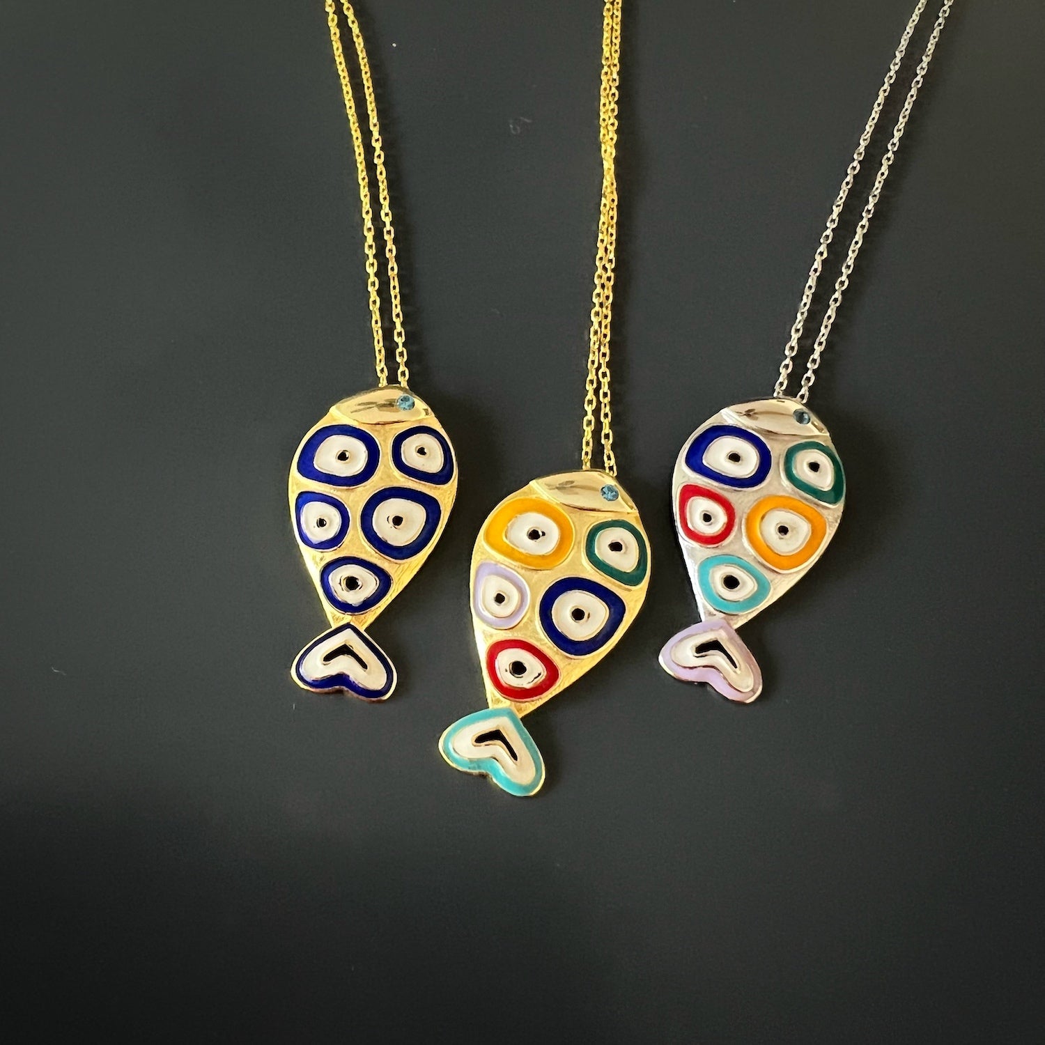 Gold Evil Eye Fish Necklace - Unique accessory featuring a gold plated fish pendant with blue enamel, accented by intricate evil eye motifs, offering both style and spiritual significance.