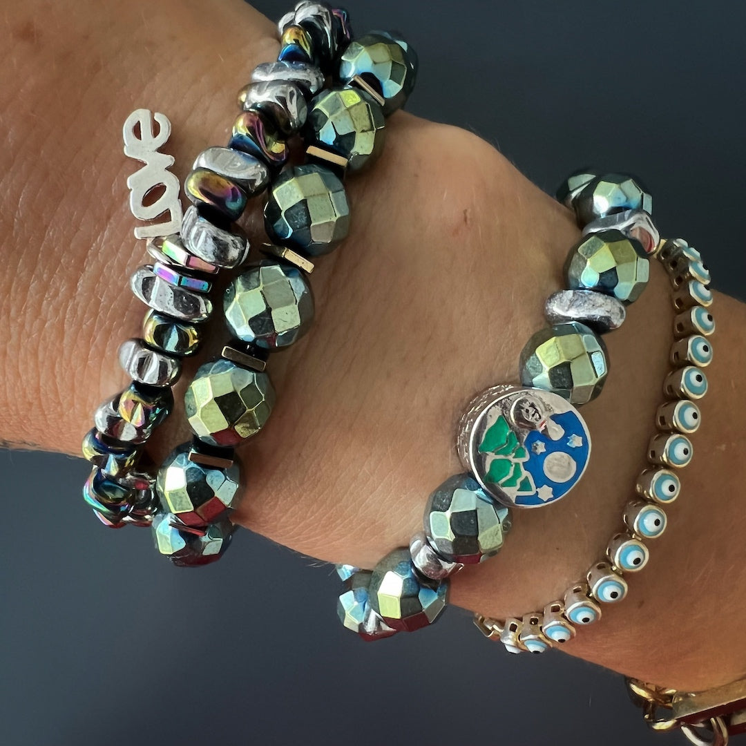 Complete your ensemble with the Hematite Love Bracelet, adding a touch of love and charm, as shown by the hand model.