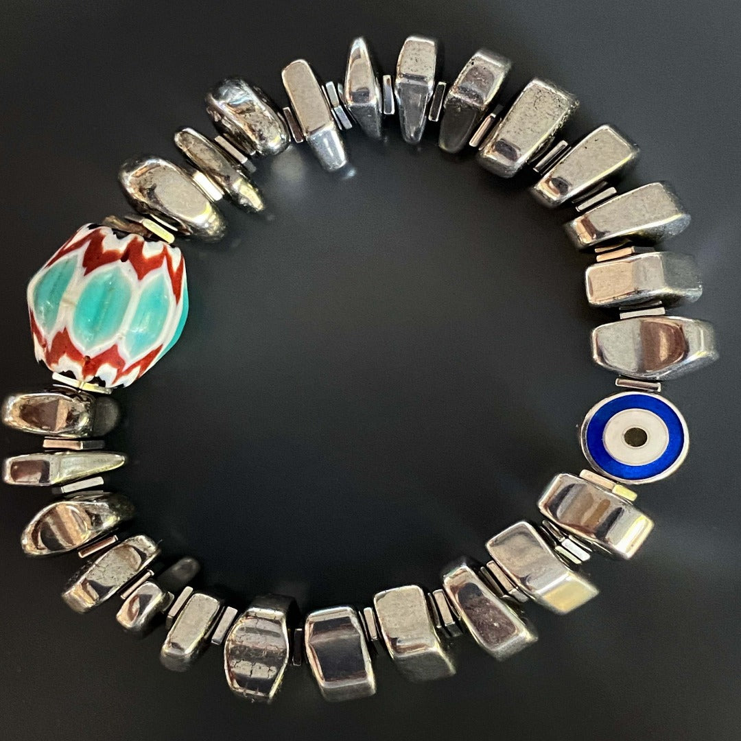 A stunning display of the Juno Bracelet, featuring silver color nugget hematite stone beads and a handmade Turquoise and Red Nepal bead, perfect for adding both style and symbolism to any outfit.