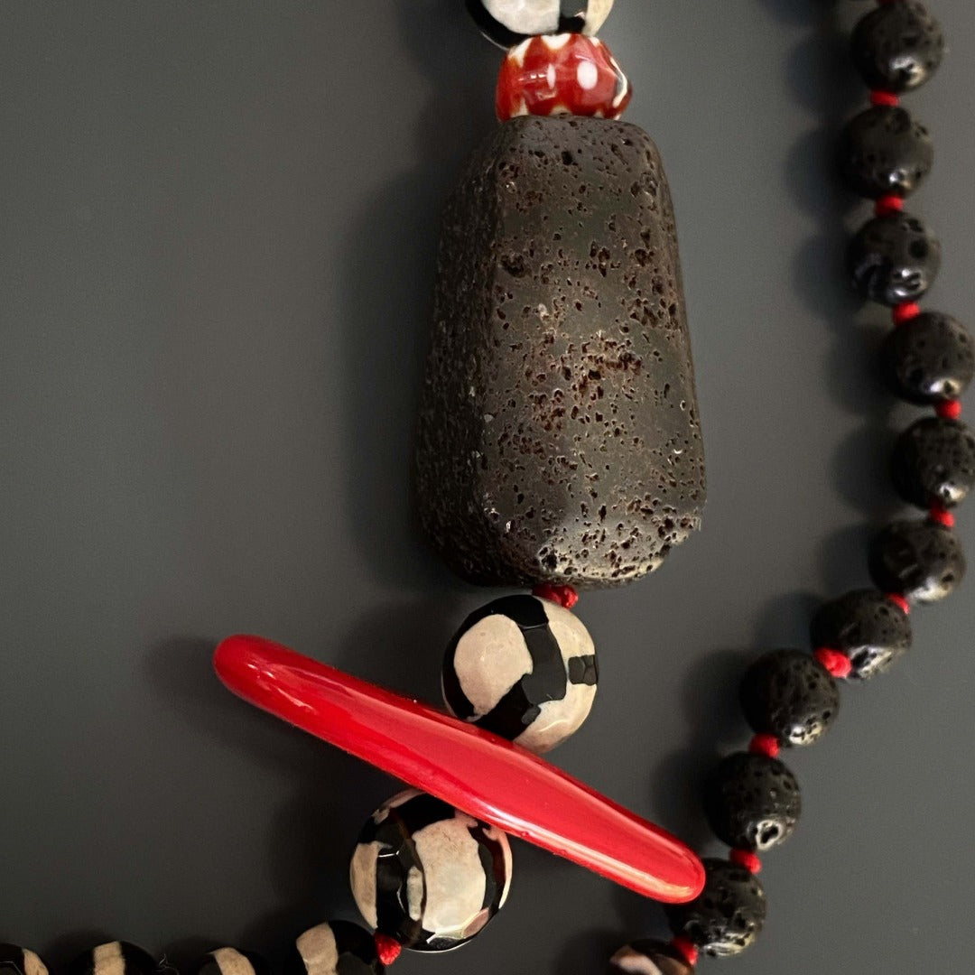 The combination of red enamel, black lava rock beads, and a handmade tassel creates a captivating design in the Lotus Flower Necklace.