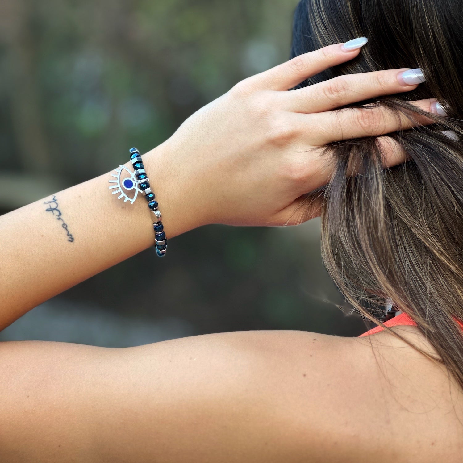 The hand model elegantly showcases the Nazar Bracelet, highlighting its beautiful blue and silver hematite stones.