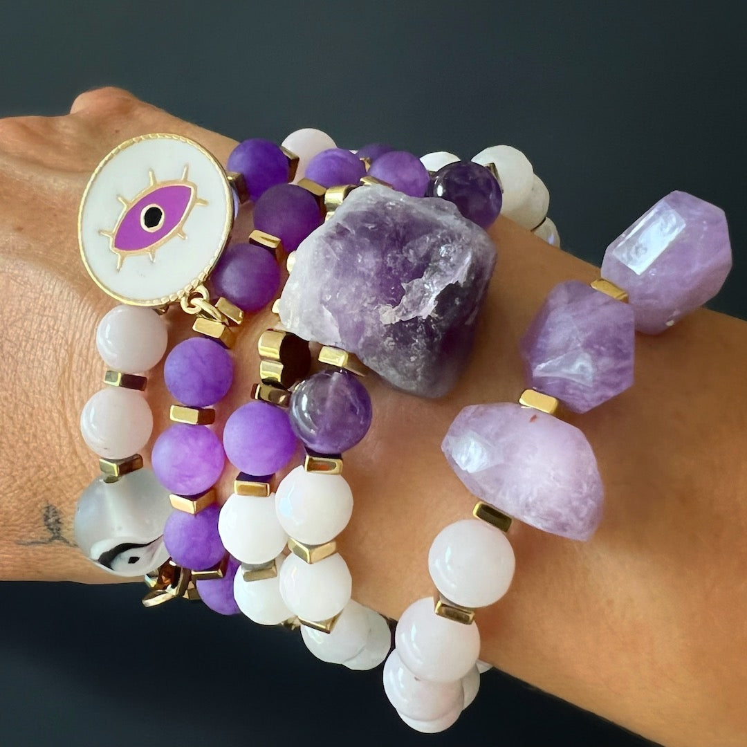 The Peaceful Mind Bracelet Set complements the hand model&#39;s style with grace and serenity, showcasing the rose quartz and amethyst beads, a glass evil eye bead, and a bronze Dream mantra charm.
