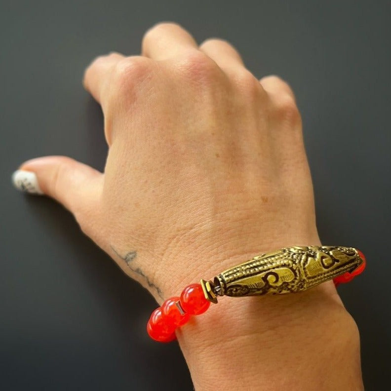Experience the energy and allure of the Red Carnelian Vintage Bracelet as it graces the hand model&#39;s wrist, featuring vibrant carnelian stone beads and a captivating Nepal brass charm.
