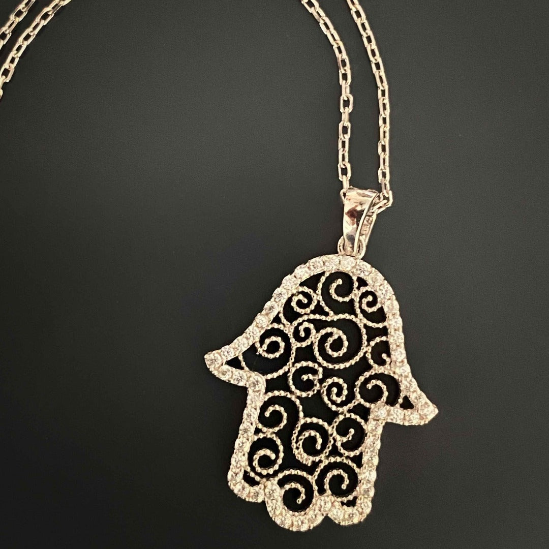 The Spiral Hamsa Necklace is a meaningful and stylish accessory, with its sterling silver chain and intricately designed Hamsa pendant adorned with sparkling CZ diamonds, symbolizing protection and blessings.
