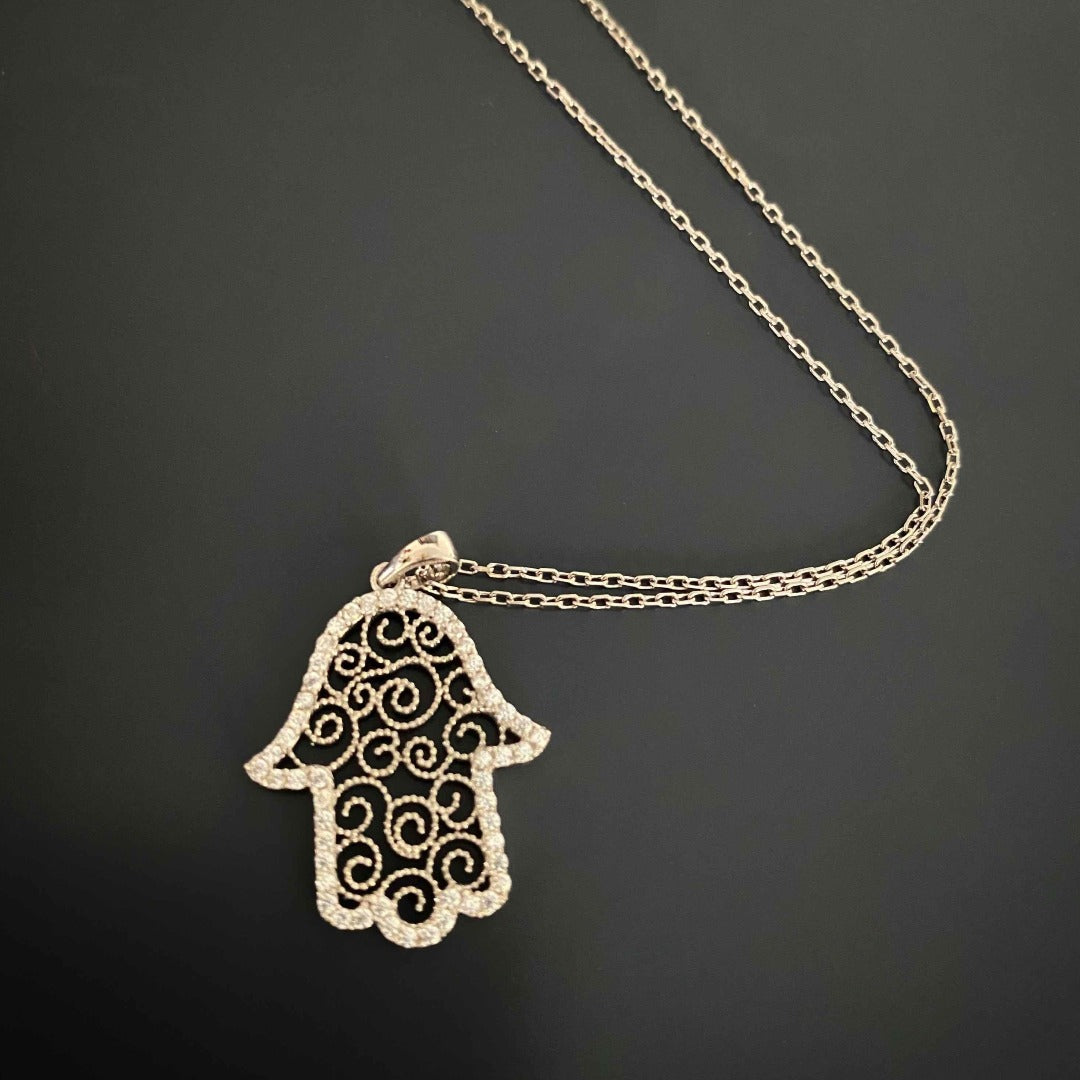 Experience the elegance and spiritual significance of the Spiral Hamsa Necklace, showcasing a beautifully crafted Hamsa pendant with intricate spiral figures and CZ diamonds.