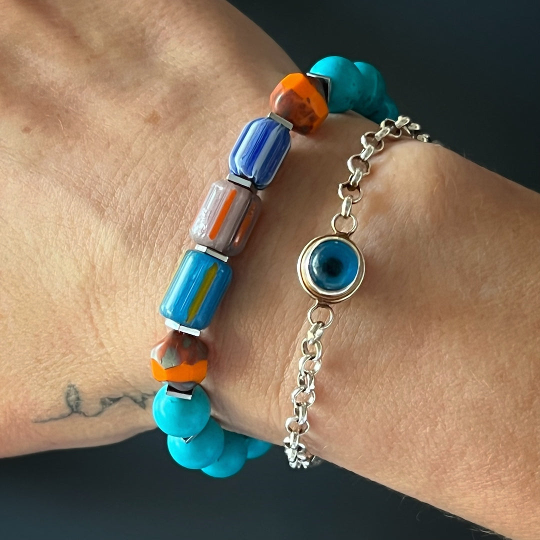 The hand model showcases the beauty and tropical charm of the Tropical Vibes Evil Eye Bracelet, featuring turquoise stone beads, African beads, and a silver evil eye bead.