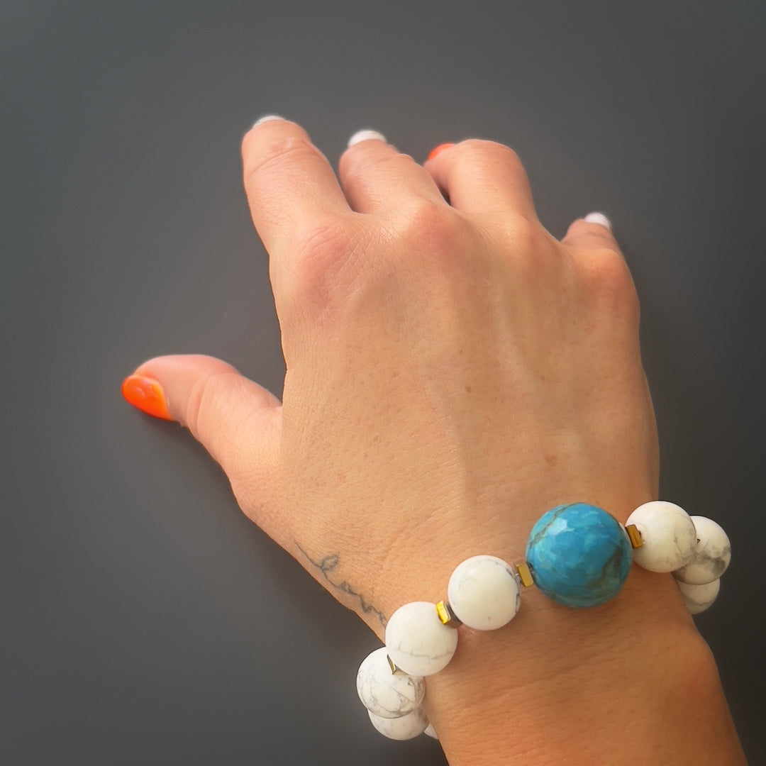 Hand model showcases the elegance and beauty of the Turquoise Balance Bracelet, adorned with turquoise, howlite, and red coral stones.