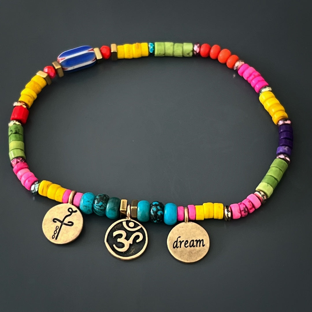 Cultivate a sense of peace and fulfillment with the Yogi Dream Anklet, showcasing bronze gold-plated Om-Dream and Heal charms, turquoise stone beads, and vibrant howlite stone beads, a harmonious combination for your spiritual well-being.