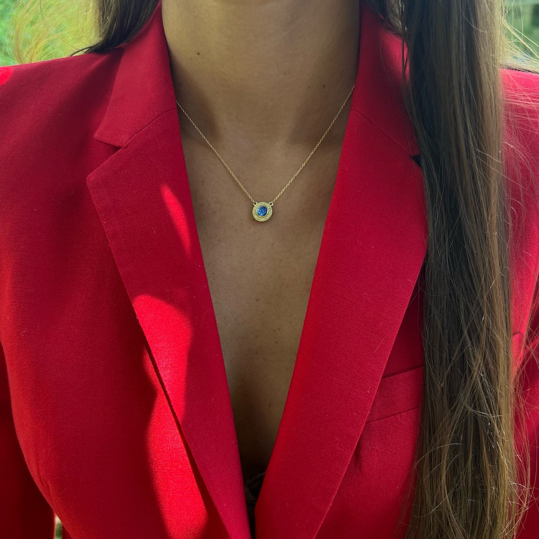 Model wearing the stunning 18k yellow gold necklace with a vibrant sapphire and sparkling diamonds, adding a touch of opulence and allure to her ensemble.