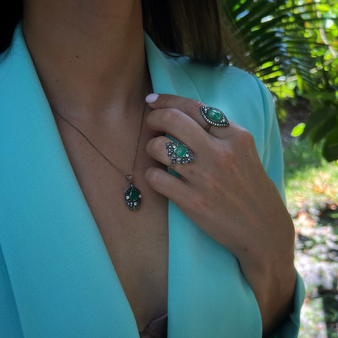 Hand model showcasing the intricate details of the Emerald &amp; Diamond Eye Ring, featuring a captivating emerald and a halo of diamonds that symbolize faithfulness and innocence.
