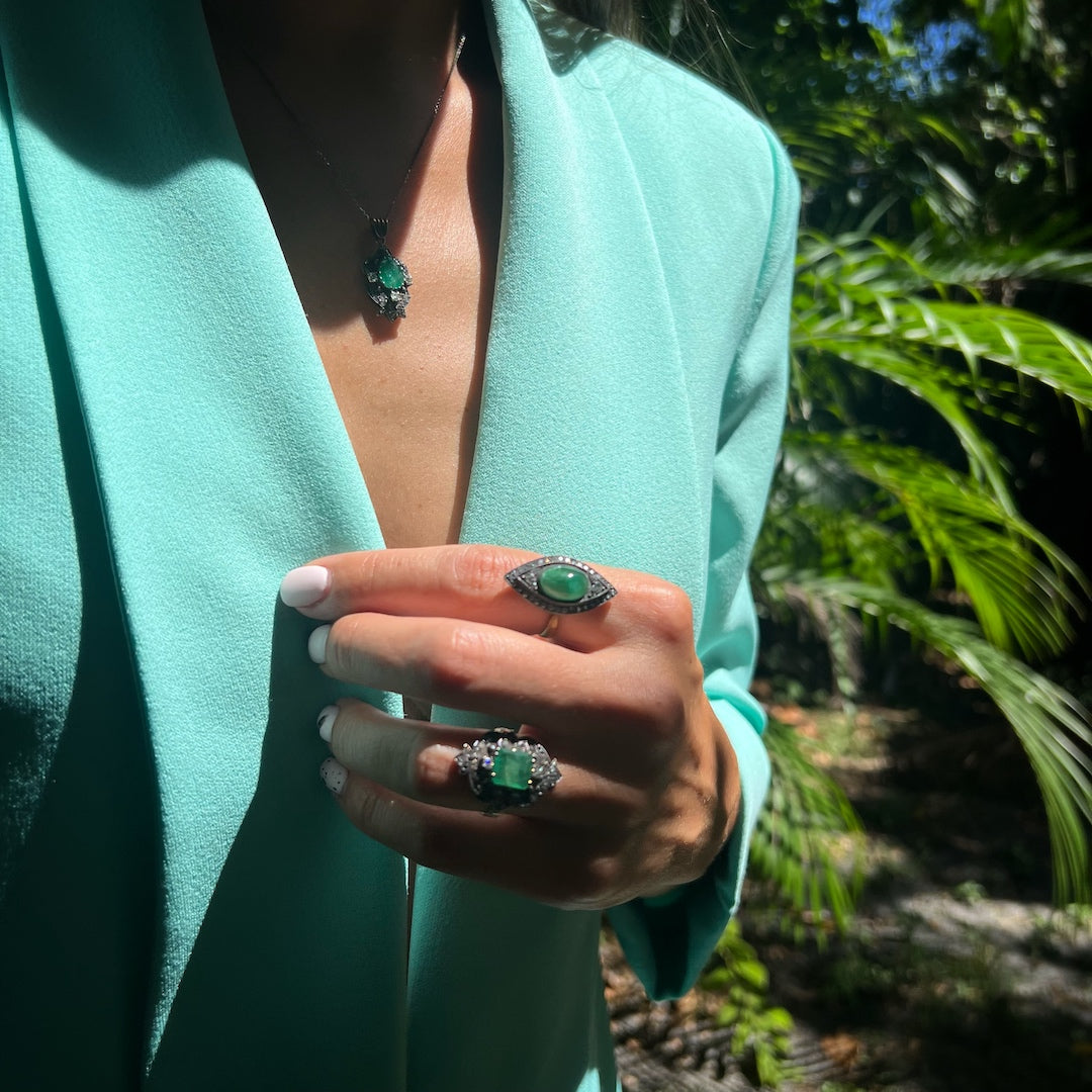 A hand model adorns the Emerald Vintage Ring, showcasing the unique and handcrafted design, which perfectly captures the essence of renewal and growth represented by the vibrant green emerald, surrounded by sparkling diamonds for an extraordinary and eye-catching effect.