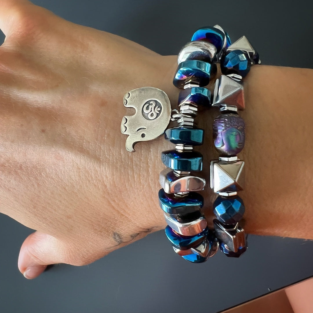 Hand model proudly wearing the Energy of Buddha Bracelet - A statement piece that features hematite pyramid beads, blue faceted hematite beads, and a serene hematite Buddha bead, representing protection and enlightenment. This bracelet adds a touch of spirituality and style to any outfit.