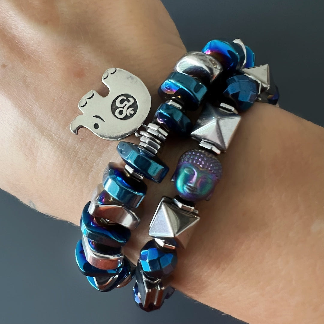 Hand model showcasing the Energy of Buddha Bracelet - An eye-catching bracelet crafted with hematite pyramid beads, blue faceted hematite beads, and a beautiful hematite Buddha bead, designed to bring positive energy and balance to the wearer.