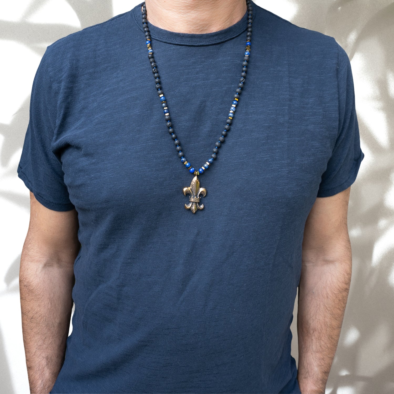 Model wearing Fleur de Lis Unique Necklace - Handmade jewelry with lava rock and lapis lazuli beads, and a bronze pendant, showcasing style, spirituality, and connection with nature.
