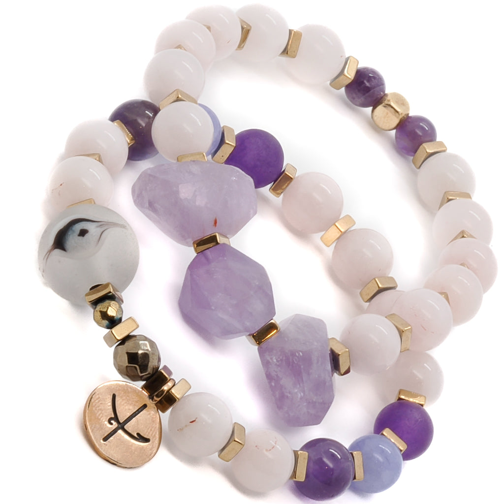 Experience the calming energy of the Peaceful Mind Bracelet Set, adorned with rose quartz and amethyst beads, a glass evil eye bead, and a bronze Dream mantra charm.