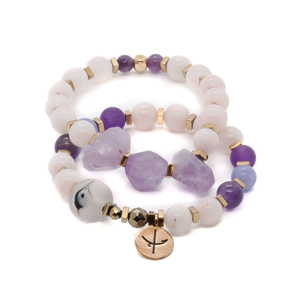 Embrace inner peace and tranquility with the Peaceful Mind Bracelet Set, featuring rose quartz and amethyst beads, a glass evil eye bead, and a bronze Dream mantra charm.
