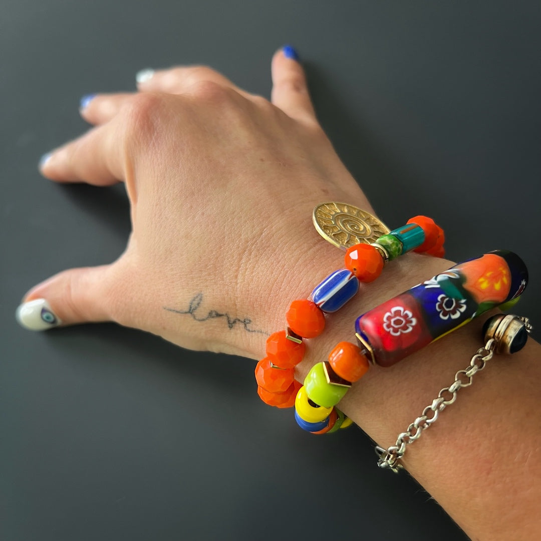The hand model effortlessly showcases the vibrant energy of the Spring Vibes Bracelet, adorned with colorful Indian beads, gold hematite spacers, and a unique glass tube bead with floral patterns.