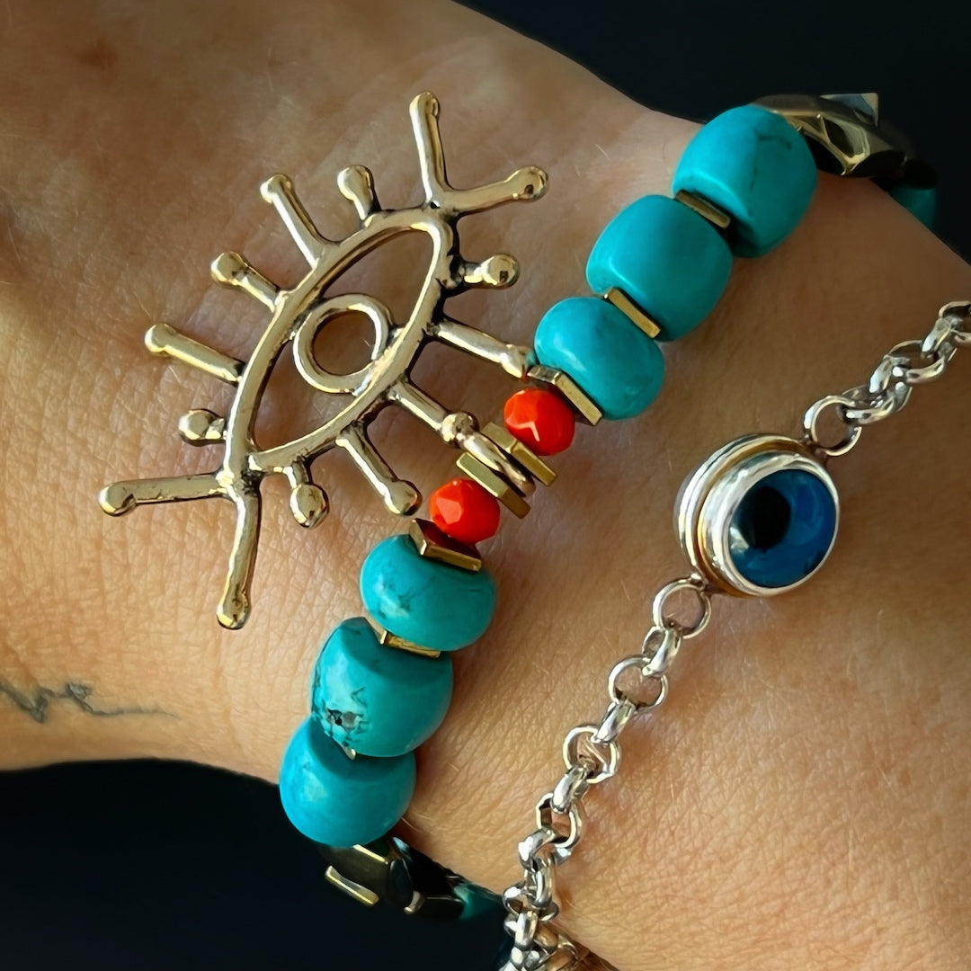 The hand model wears the Turquoise Long Lash Bracelet, showcasing the elegance of turquoise beads, a sparkling Swarovski crystal, hematite, and a brass evil eye charm.
