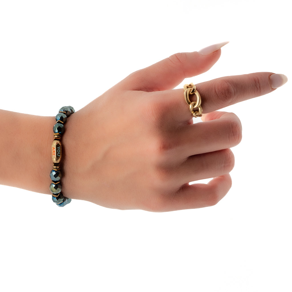 See the You Are Loved Bracelet adorning the hand model&#39;s wrist, highlighting the grounding energy of the green hematite stone beads and the precious &quot;You Are Loved&quot; tube bead.