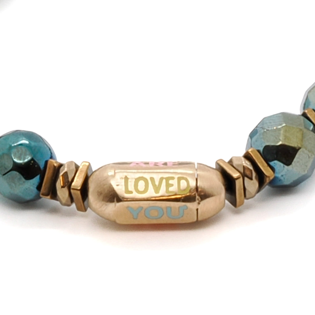 Discover the beauty and meaning of the You Are Loved Bracelet, adorned with green hematite stone beads and a precious "You Are Loved" tube bead.